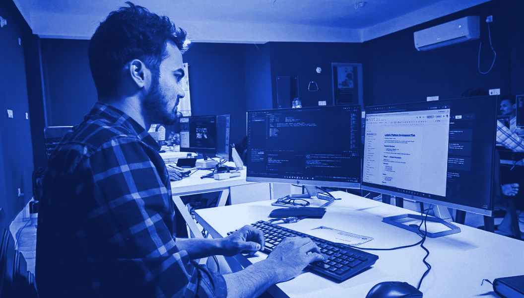 A developer working at code on multiple monitors in a dark room